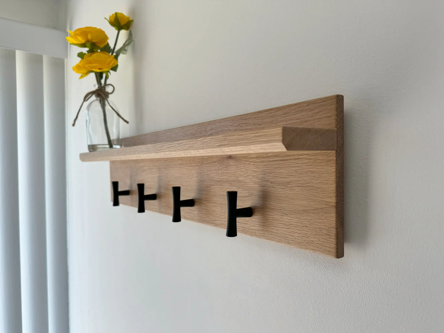 White oak wall mounted coat rack with shelf, matte black t hooks, front angled view 