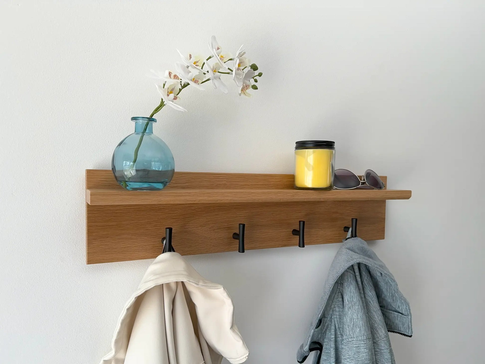 White oak wall mounted coat rack, matte black t hooks, angled view in use 