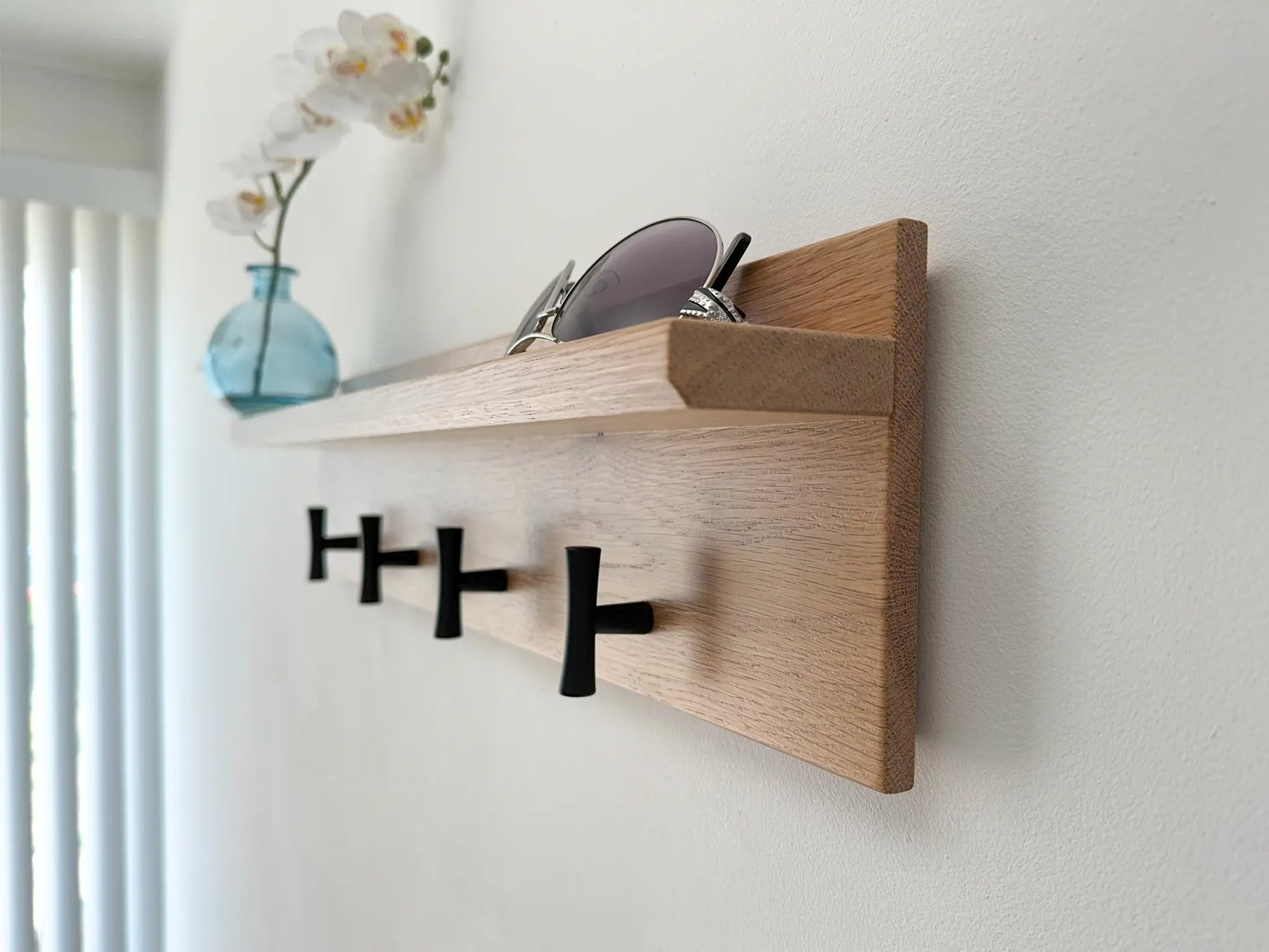 White oak coat rack with shelf, matte black t hooks, angled view in use