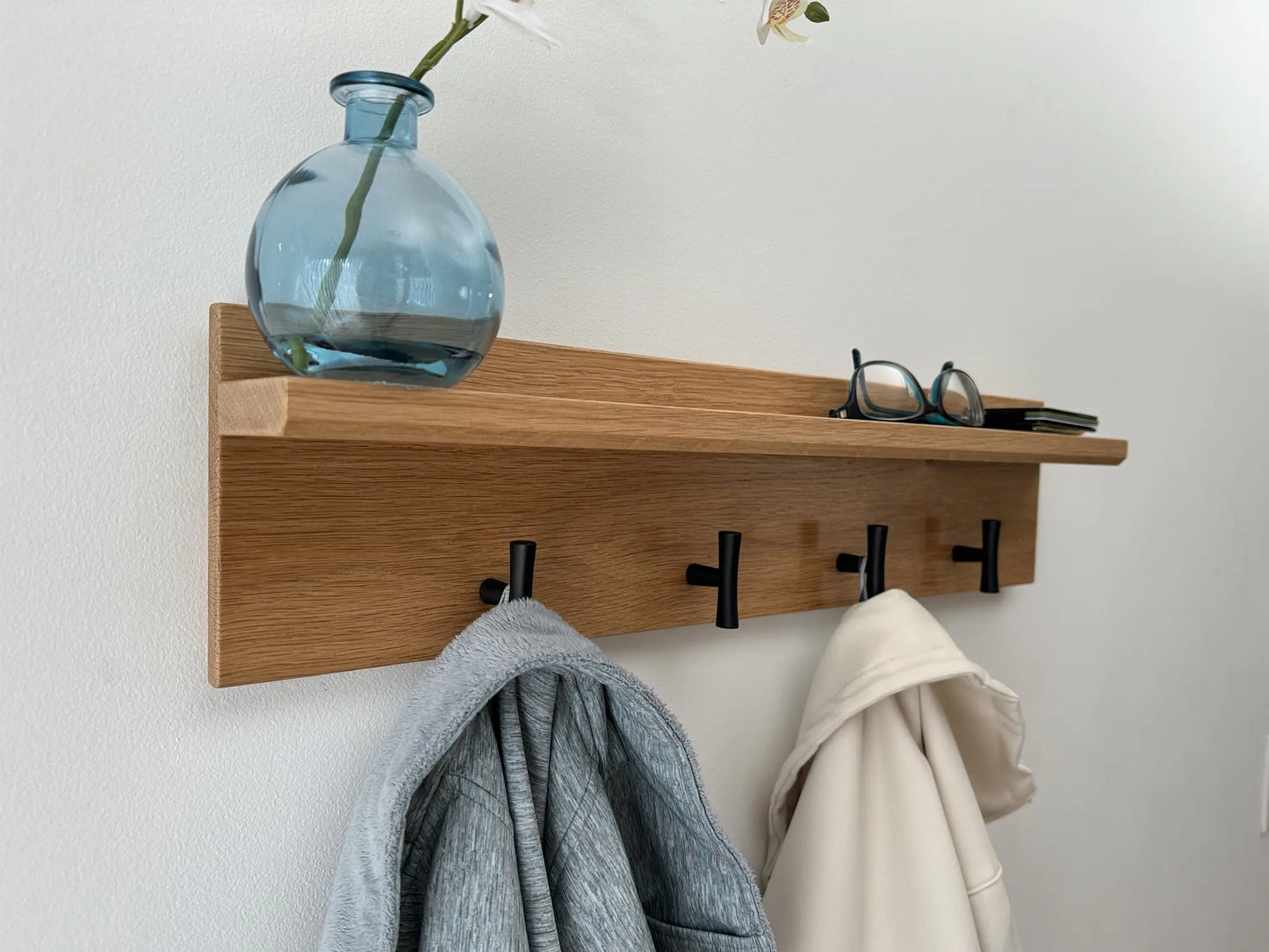 White oak wall mounted coat rack with shelf, matte black t hooks, angled view in use